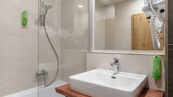 A bathroom with a shower, a sink, a mirror, and a wooden shelf.