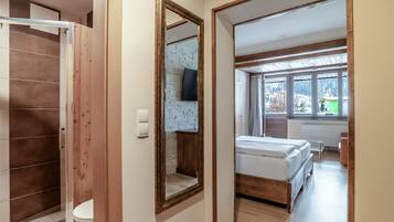 A hotel room with a wooden wardrobe, a mirror, a bed, a window with a view of a snowy landscape, and a mounted television.