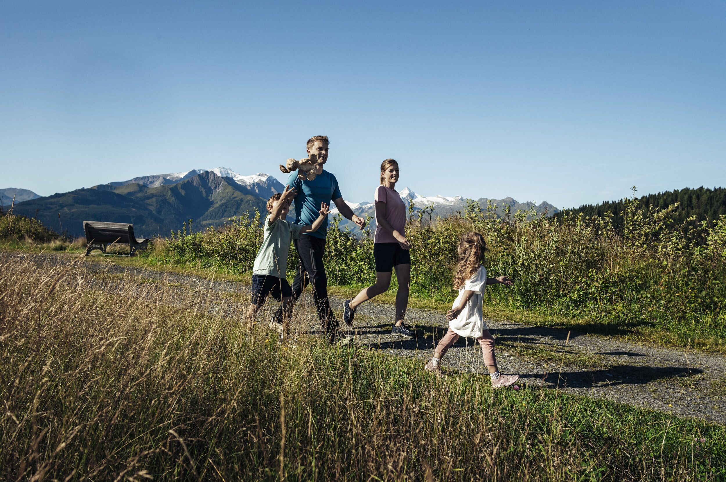 Une famille se promène sur un chemin de gravier, avec une chaîne de montagnes en arrière-plan.