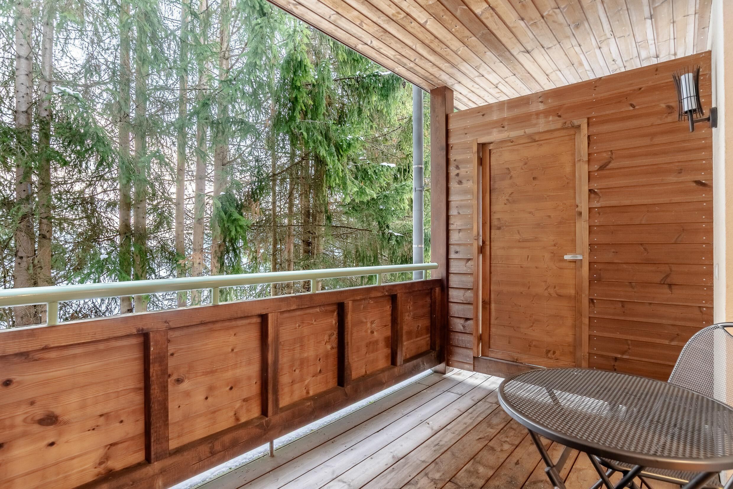 Une terrasse en bois avec une table et une chaise en métal, une porte en bois et une vue sur les arbres.