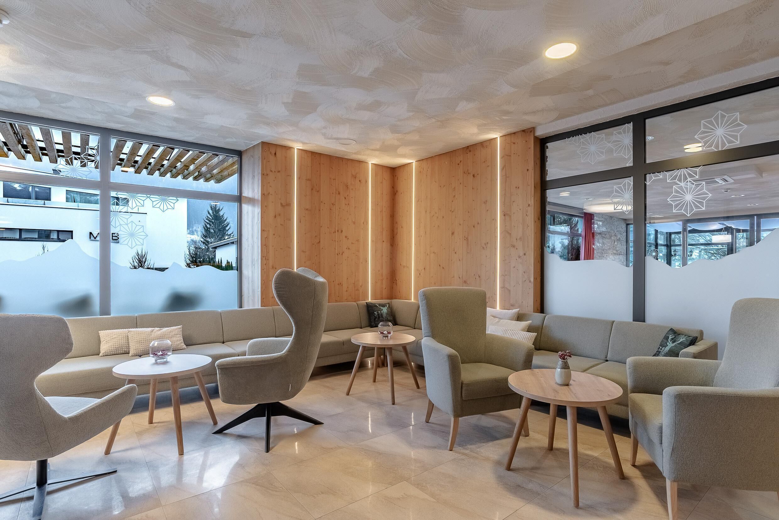 Un interior moderno con un sofá, sillones y mesitas, paredes de paneles de madera y ventanas amplias con vistas.