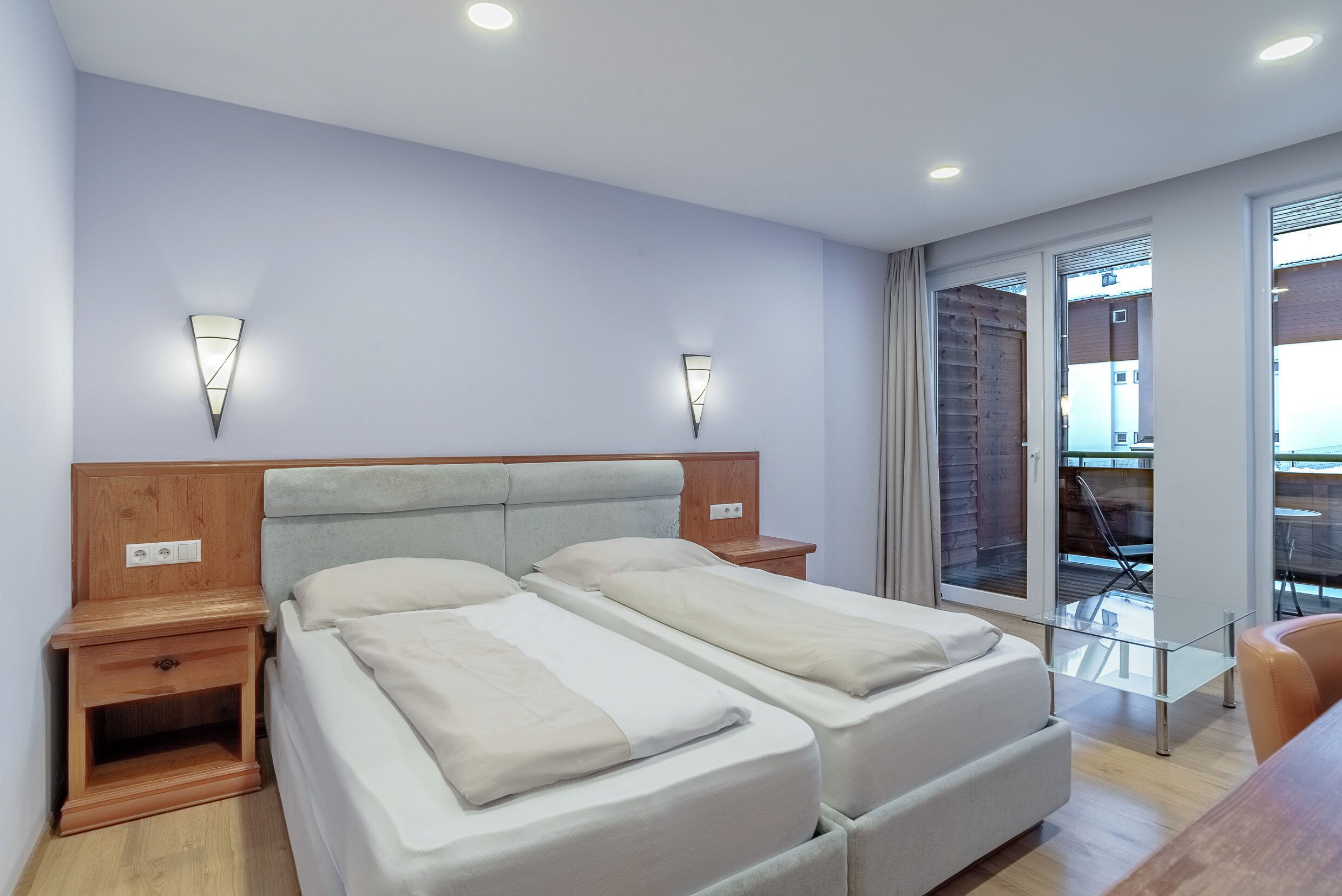 A double bed with a wooden headboard, two bedside tables with lamps, and a sliding glass door leading to an outdoor area.