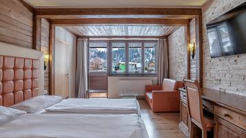 Habitación de hotel con cama, sofá, televisión y vistas a la montaña.