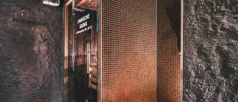 A sauna room with a wooden door, tiled walls, and two lit candles on the floor.