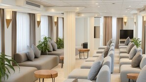 Un vaste espace de vie comprenant plusieurs canapés et fauteuils, un téléviseur à écran plat et une grande fenêtre avec des rideaux.