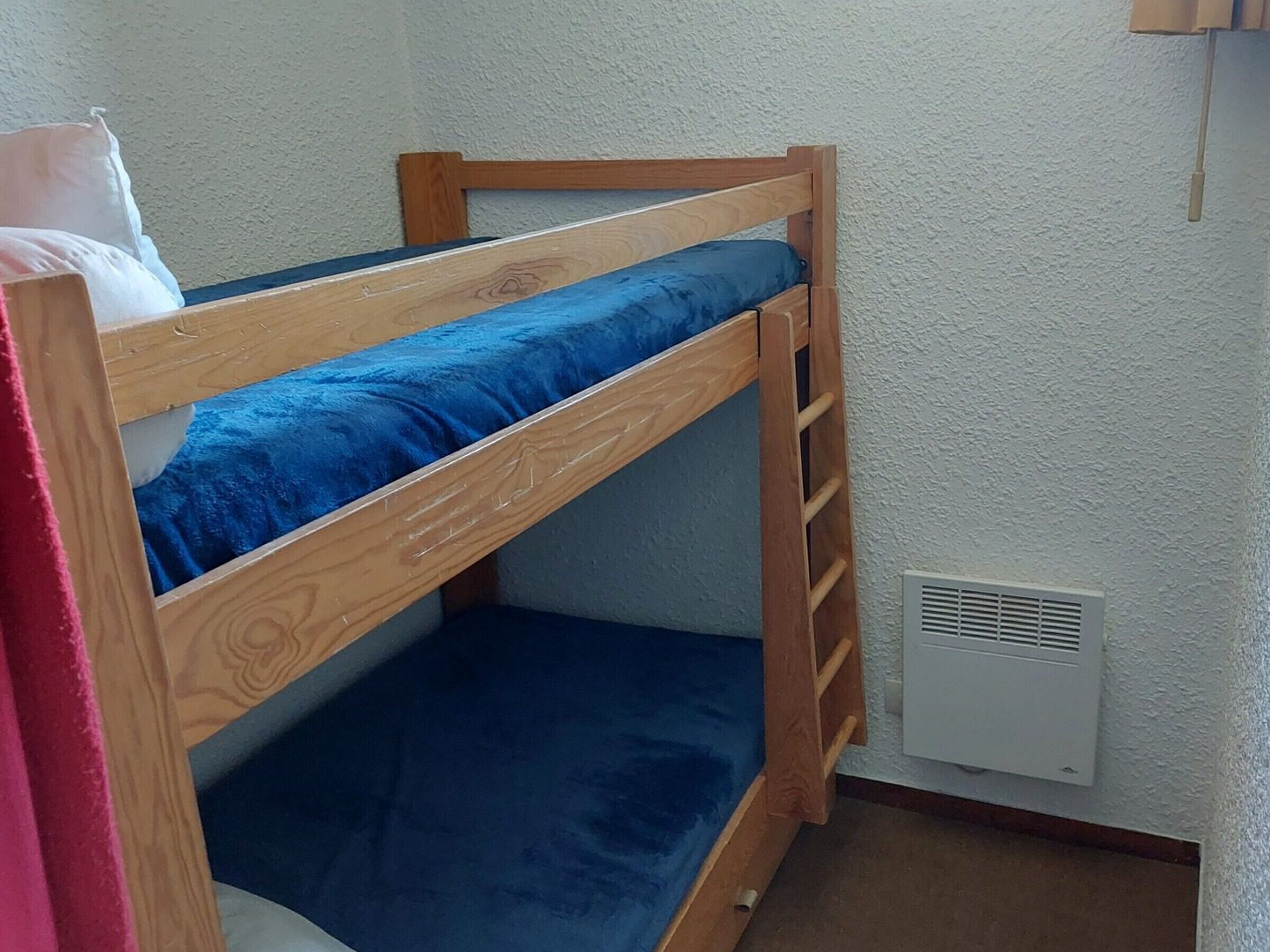 A bunk bed with blue bedding in a room with white walls and a white vent.