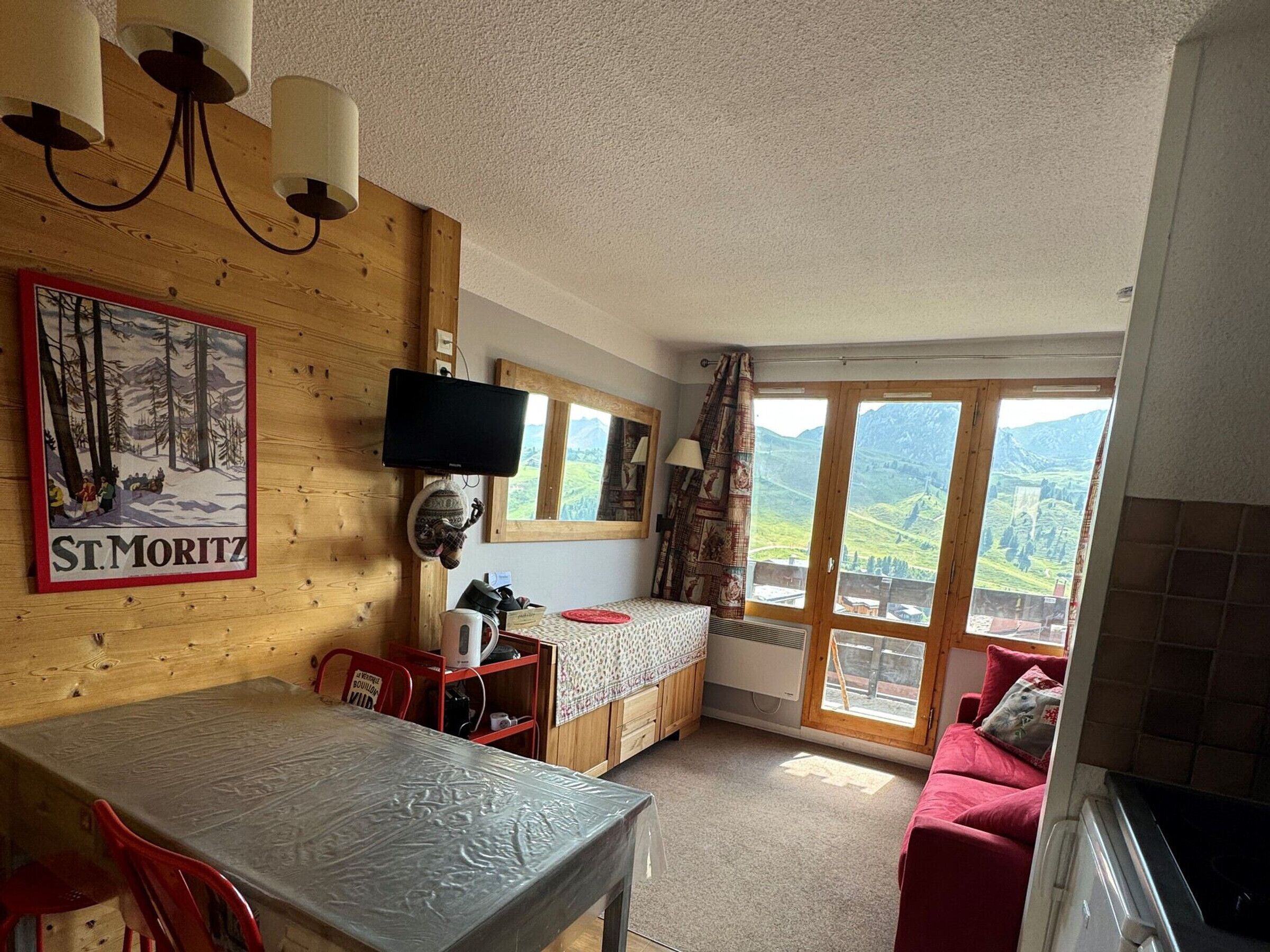 Una habitación acogedora con una pared de madera, una cama, una mesa y vistas a las montañas a través de ventanas amplias.