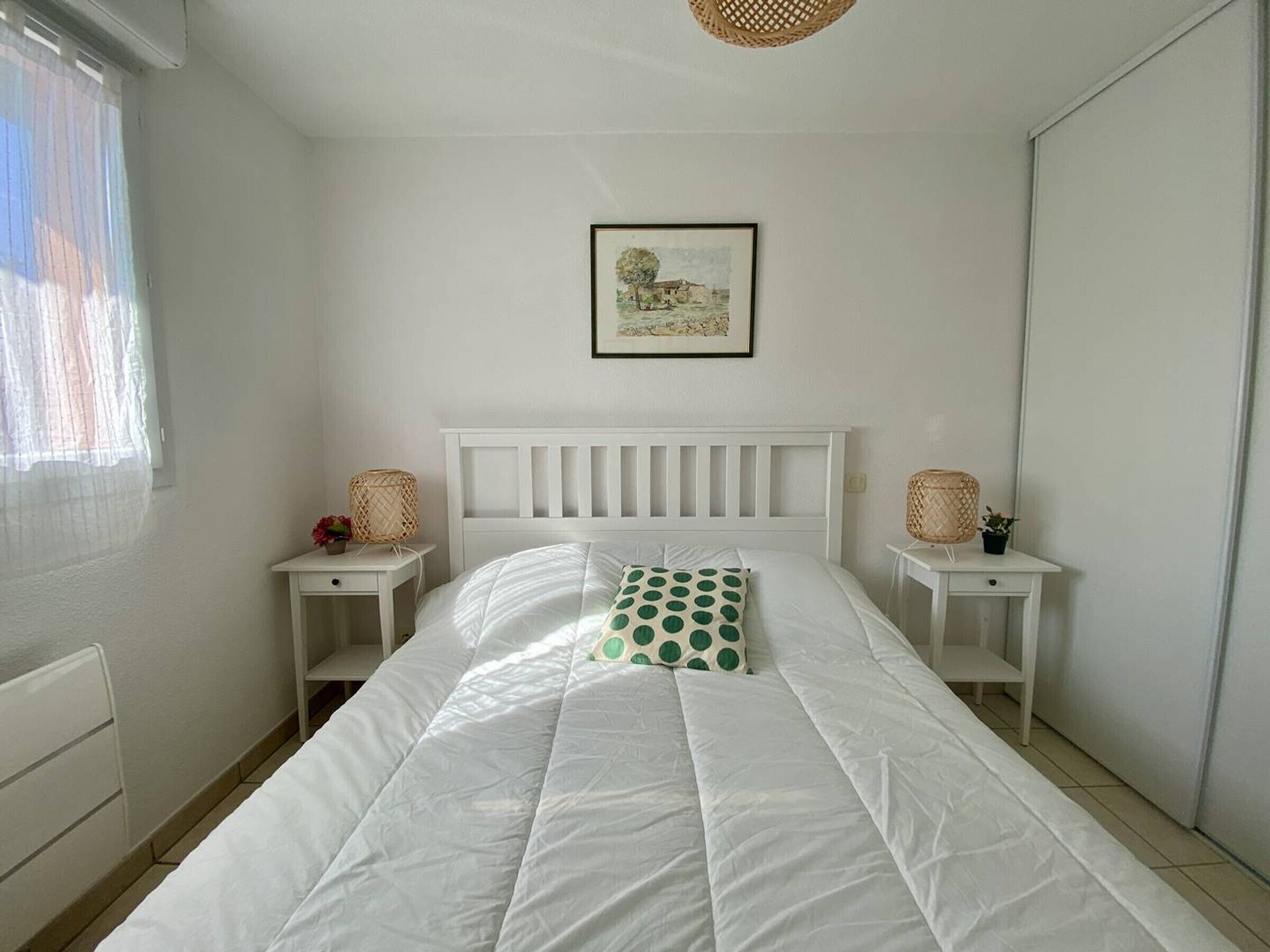 Ein Schlafzimmer mit einem weißen Bett, einem gerahmten Bild an der Wand und zwei Nachttischen mit Lampen.