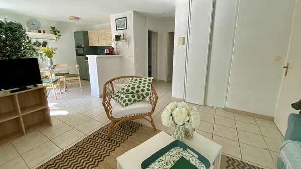 A living room with a television, a wicker chair, a coffee table, and a kitchen in the background.