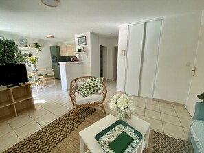 A living room with a television, a wicker chair, a coffee table, and a kitchen in the background.