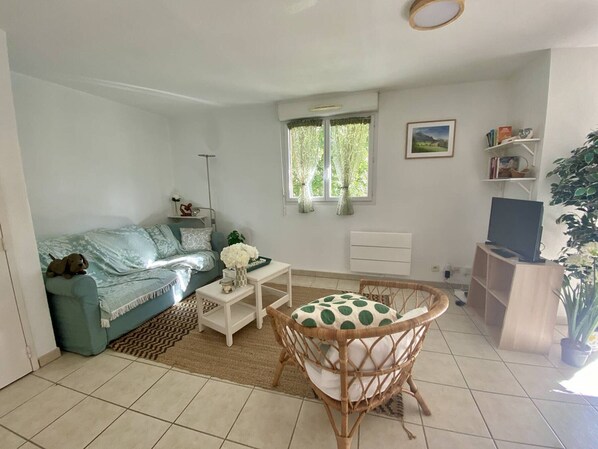 A living room with a sofa, a coffee table, a wicker chair, a television, and a bookshelf.