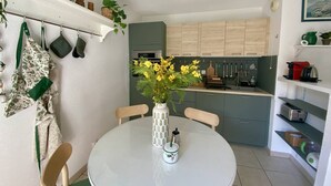 A modern kitchen with a round dining table, a vase of yellow flowers, and a clock on the wall.