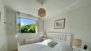 A bedroom with a bed, a bedside table, a window, and a hanging light fixture.