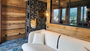Een houten interieur met een bank, een decoratieve wand met een ronde spiegel, en een groot raam met uitzicht op de omgeving.