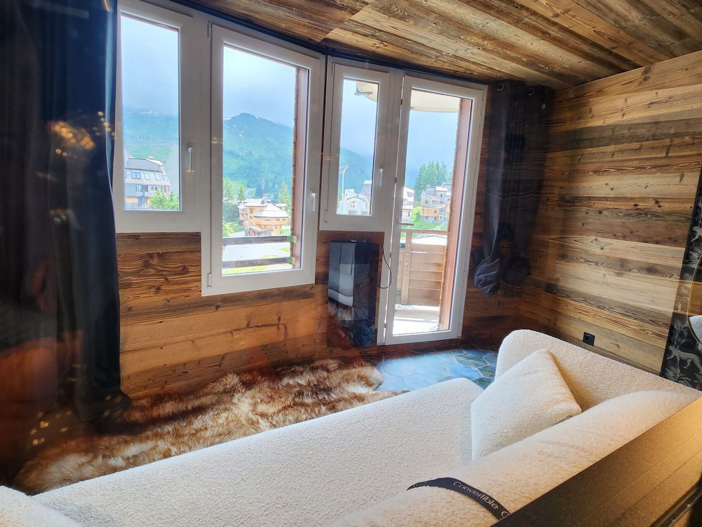 Una habitación con sofá, televisión y vistas a un paisaje montañoso a través de ventanas amplias.