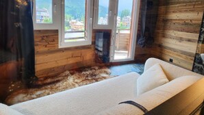 Een knus ingerichte kamer met een bank, een televisie en grote ramen met uitzicht op de omgeving.