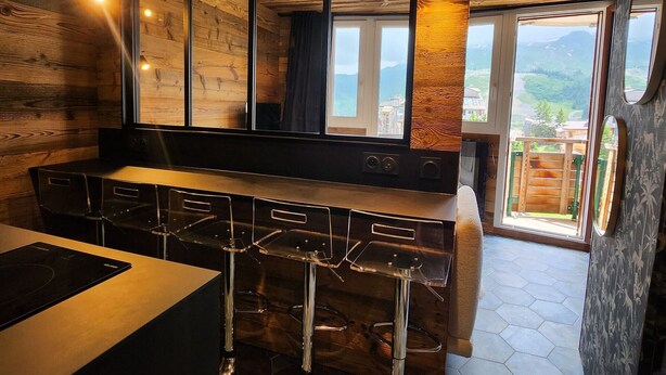 Een moderne keuken met houten details, een bar met krukken en grote ramen met uitzicht op het landschap.