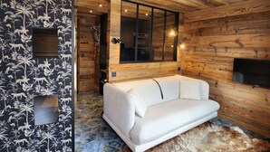 Een gezellige kamer met een witte bank, houten wanden, een groot raam en een aan de muur bevestigde televisie.