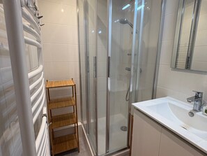 Un baño moderno con cabina de ducha de vidrio, estante de madera y lavamanos blanco.