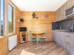 A compact kitchen with wooden walls, a dining table with chairs, a television, and a microwave.
