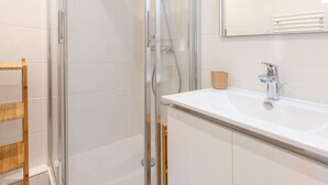 A modern bathroom with a glass-enclosed shower, a white sink with a chrome faucet, and a wooden shelf. - Cozy renovated studio for 2 in Avoriaz, view of Hauts Forts (Avoriaz)