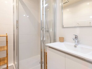 A modern bathroom with a glass-enclosed shower, a white sink with a chrome faucet, and a wooden shelf. - Cozy renovated studio for 2 in Avoriaz, view of Hauts Forts (Avoriaz)