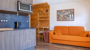 A compact living space with a kitchenette, a wooden shelf unit, a sofa, and a collage artwork on the wall. - Cozy renovated studio for 2 in Avoriaz, view of Hauts Forts (Avoriaz)