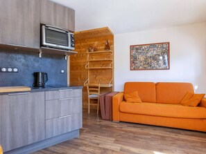 A compact living space with a kitchenette, a wooden shelf unit, a sofa, and a collage artwork on the wall. - Cozy renovated studio for 2 in Avoriaz, view of Hauts Forts (Avoriaz)