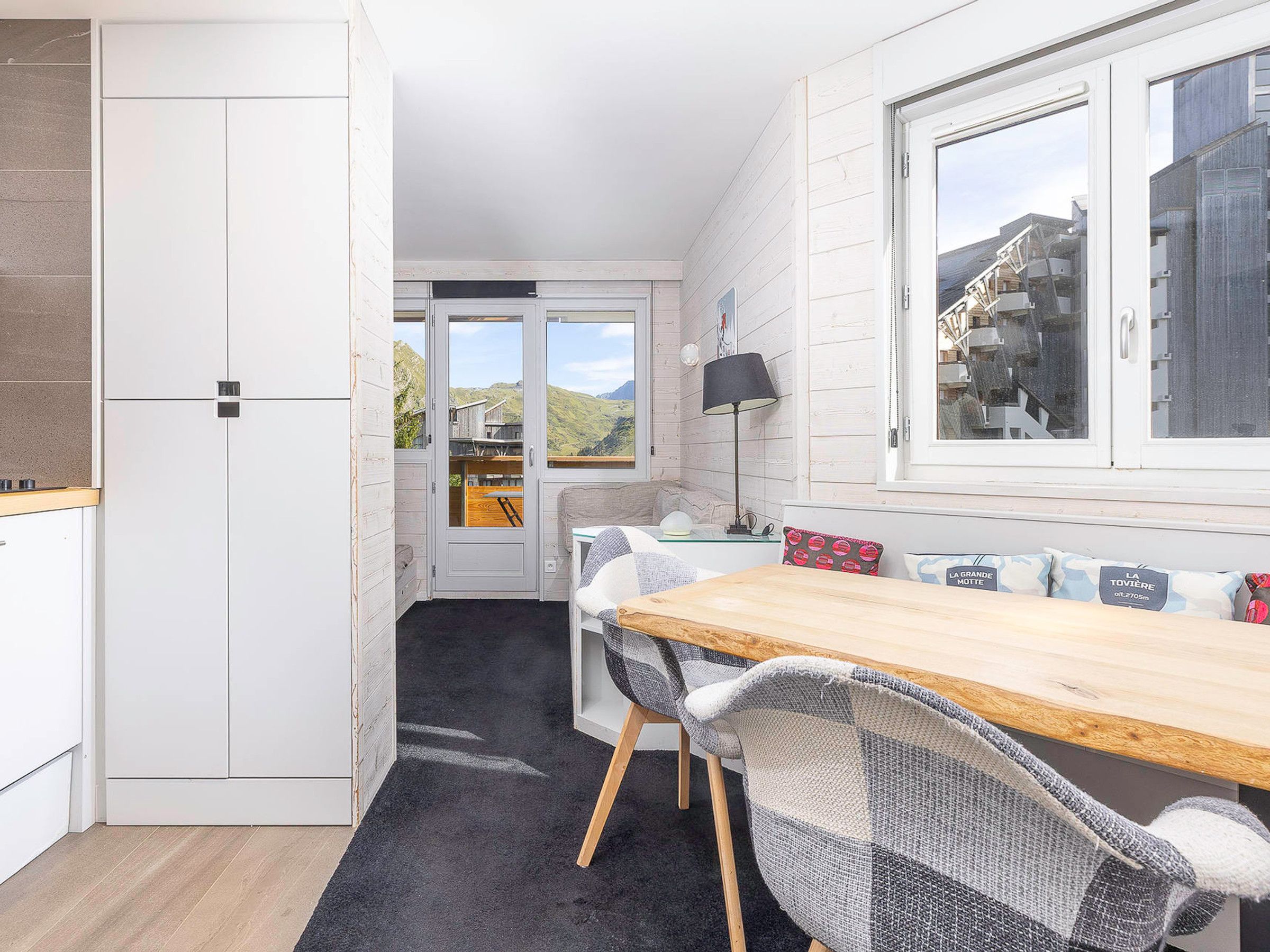 A compact kitchen with a dining area, a window with a view of a mountain, and a door leading to an outdoor area.
