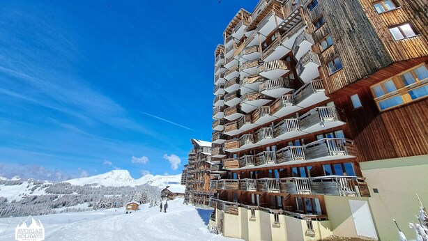 Un hotel de varios pisos con balcones y una pista de esquí al fondo.