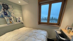 Un dormitorio con cama, escritorio y ventana con vista a árboles.