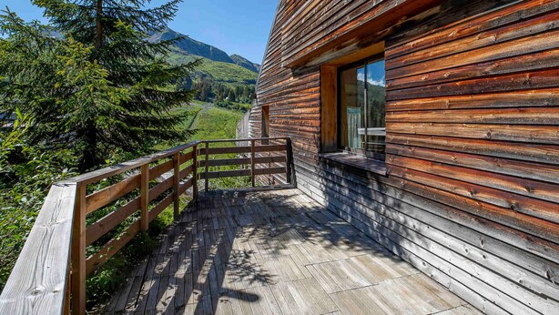 A wooden cabin with a wooden deck and a glass door, surrounded by forest and mountains. - Chalet Babayaga, 7 rooms, 12 pers, ski-in/ski-out access (Avoriaz)