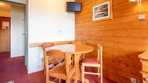 A wooden-paneled room with a round wooden table and chairs, a television mounted on the wall, and a framed picture above the table. - Studio 4 pax in Avoriaz, quiet with balcony (Avoriaz)