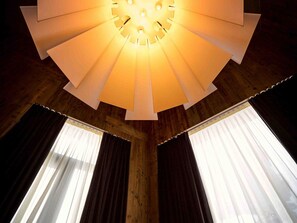 Une pièce dotée d’un plafond au design original, de murs en bois et de grandes fenêtres ornées de rideaux.