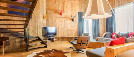 Un interior rústico con una escalera de madera, un televisor, un sofá de cuero y un tapiz de piel de vaca.