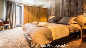 A bedroom with a large bed, a wooden wall, and a window with curtains. - Exceptional loft for 12, ski-in access, sauna & hammam (Avoriaz)
