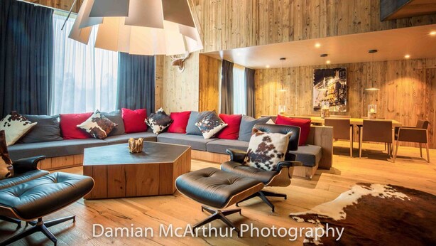 A modern living room with a wooden wall, a sofa set, a coffee table, and a dining area with chairs. - Exceptional loft for 12, ski-in access, sauna & hammam (Avoriaz)