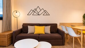 A modern living room with a brown sofa, two white round tables, a floor lamp, and a dining area with chairs.