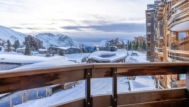 A snow-covered mountain town with wooden buildings and a wooden balcony railing.
