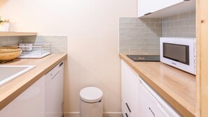 A compact kitchen with a microwave, a sink, and a small trash bin.