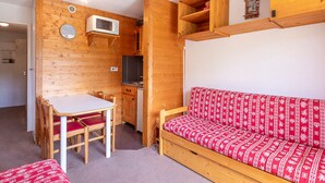 Una habitación compacta con interior de madera, una kitchenette, una mesa de comedor con sillas y un sofá con cojines estampados.