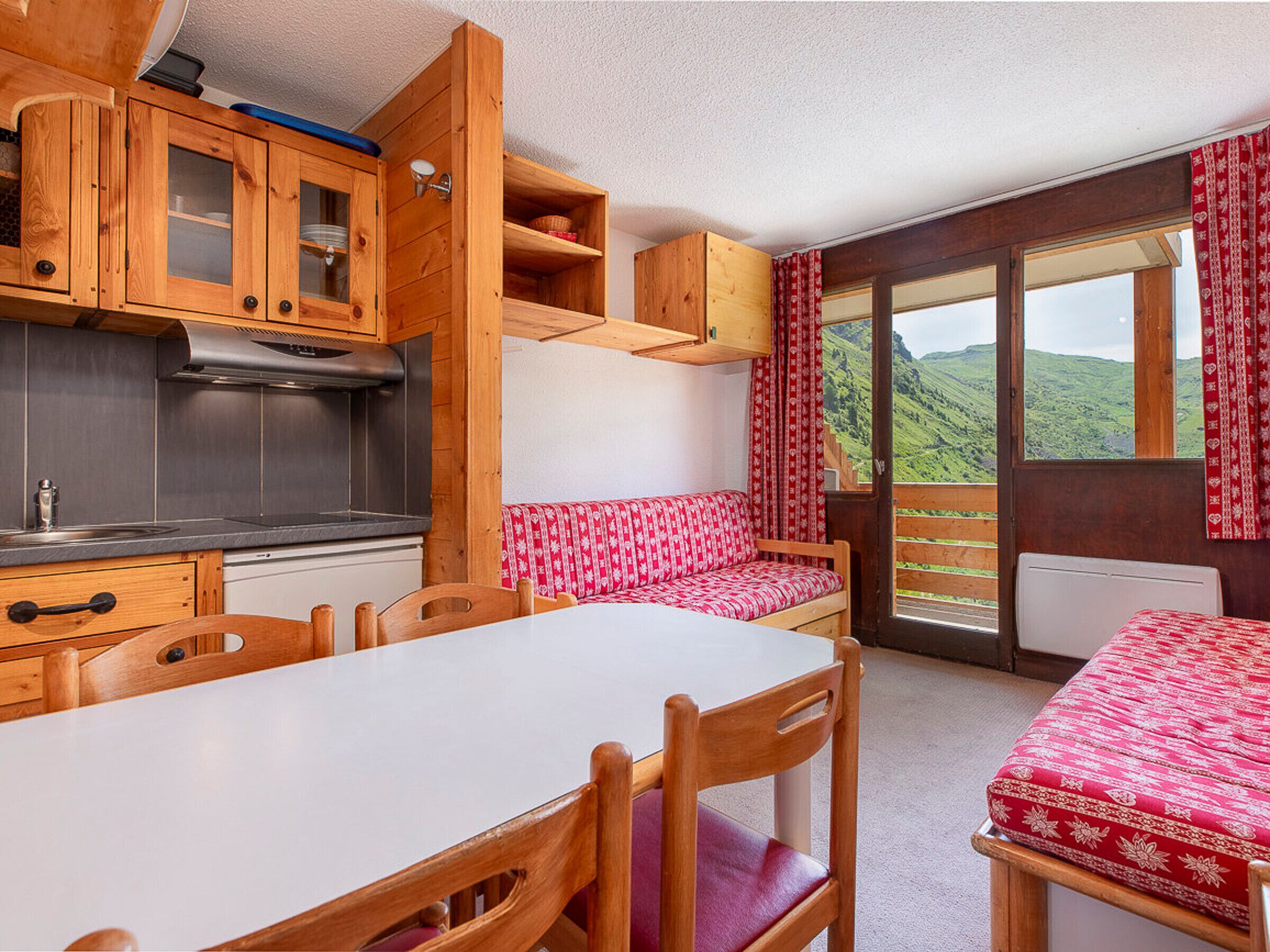 Un intérieur de chalet chaleureux, avec des meubles en bois, un coin cuisine et une vue imprenable sur les montagnes, visible à travers de grandes fenêtres.