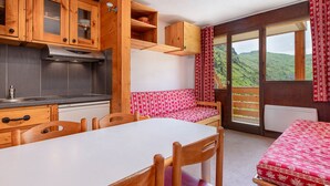 Interior acogedor de una cabaña con muebles de madera, una zona de cocina y una vista panorámica de las montañas a través de amplias ventanas.