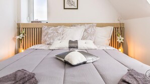A bedroom with a sloped ceiling, a bed with multiple pillows, a framed artwork on the wall, and a window with a view. - Peaceful country house with wifi and pets allowed, near cultural sites (Villedieu-les-Poêles)