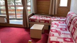 Una habitación acogedora con un sofá de madera, una mesita y vistas a un bosque a través de grandes ventanales.
