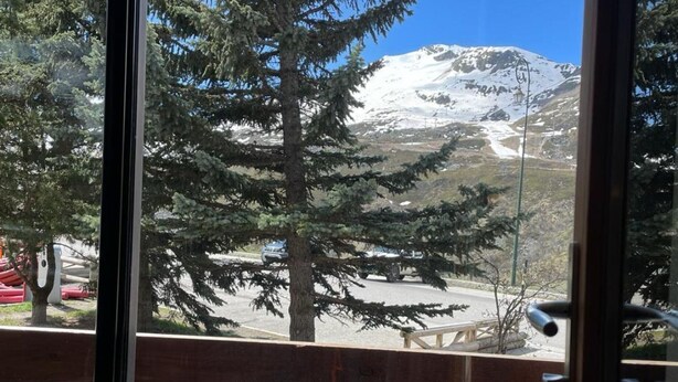 Vista de una montaña nevada a través de una ventana con barandilla de madera.