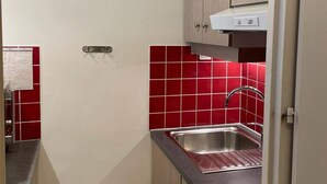 Una cocina pequeña con un lavamanos de acero inoxidable, salpicadero de azulejos rojos y armarios de madera.