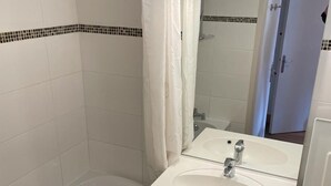 Un baño con lavamanos blanco, espejo y ducha.