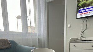 A modern living room with a glass coffee table, a white wine glass set, a blue sofa, and a television displaying a news channel.