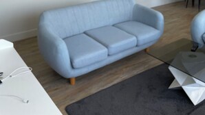 A modern living room with a light blue sofa, two framed landscape paintings, a dining area with a table and chairs, and a grey rug.